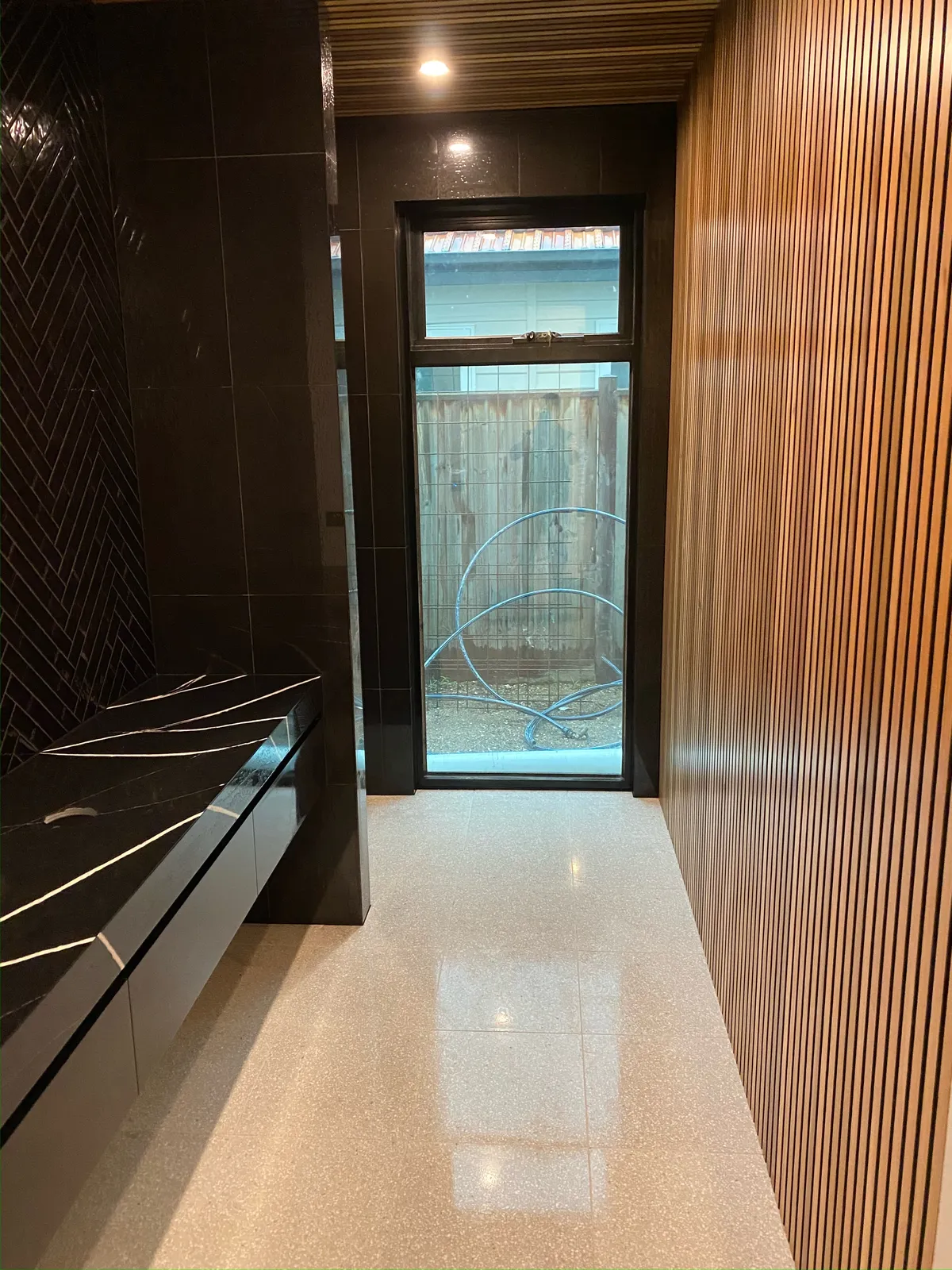 Ensuite with dark herringbone feature wall tiling, black stone vanity and terrazzo-look floor