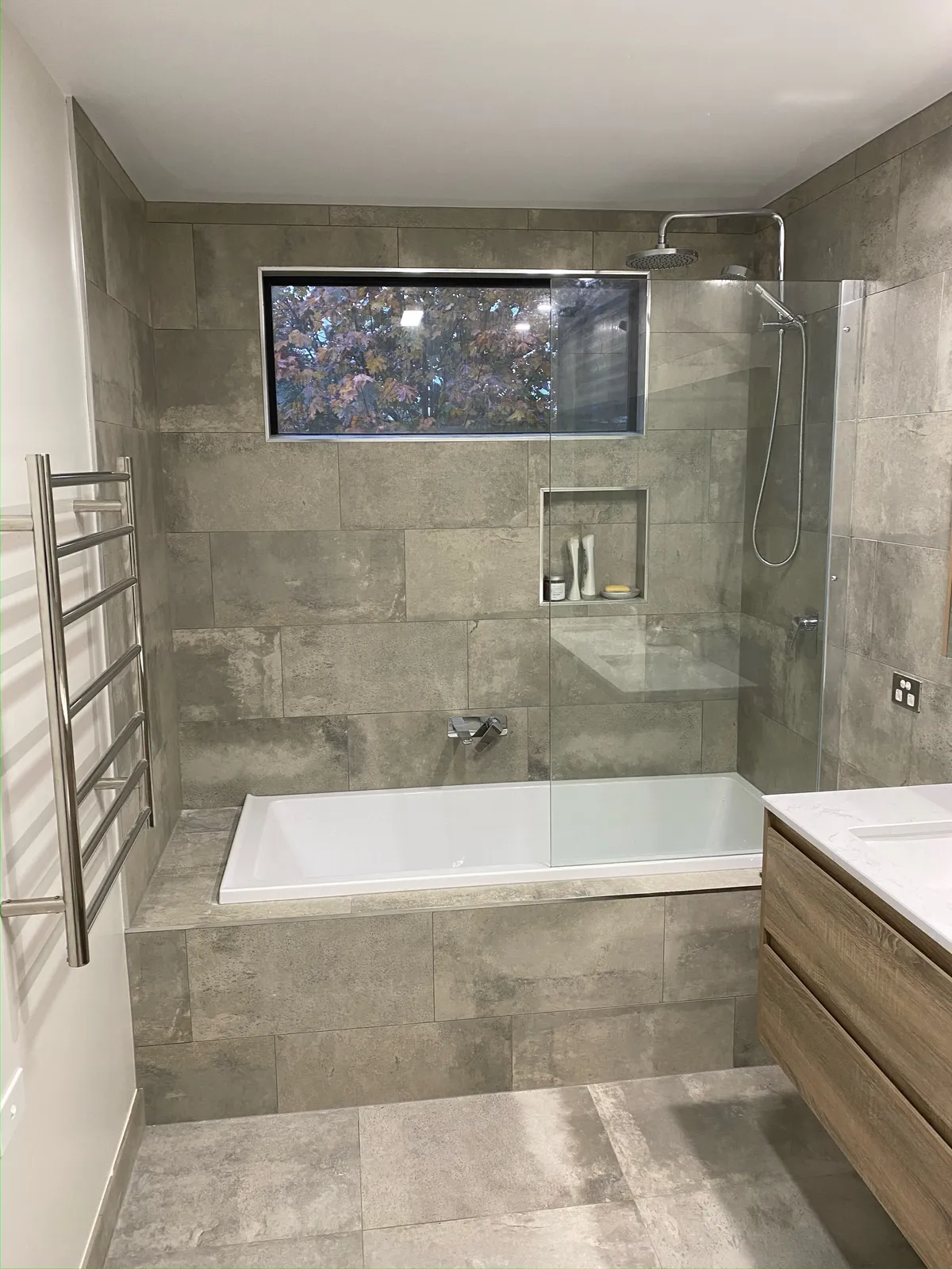 Ensuite with concrete-look tiled shower, feature mosaic window niche and inset bath