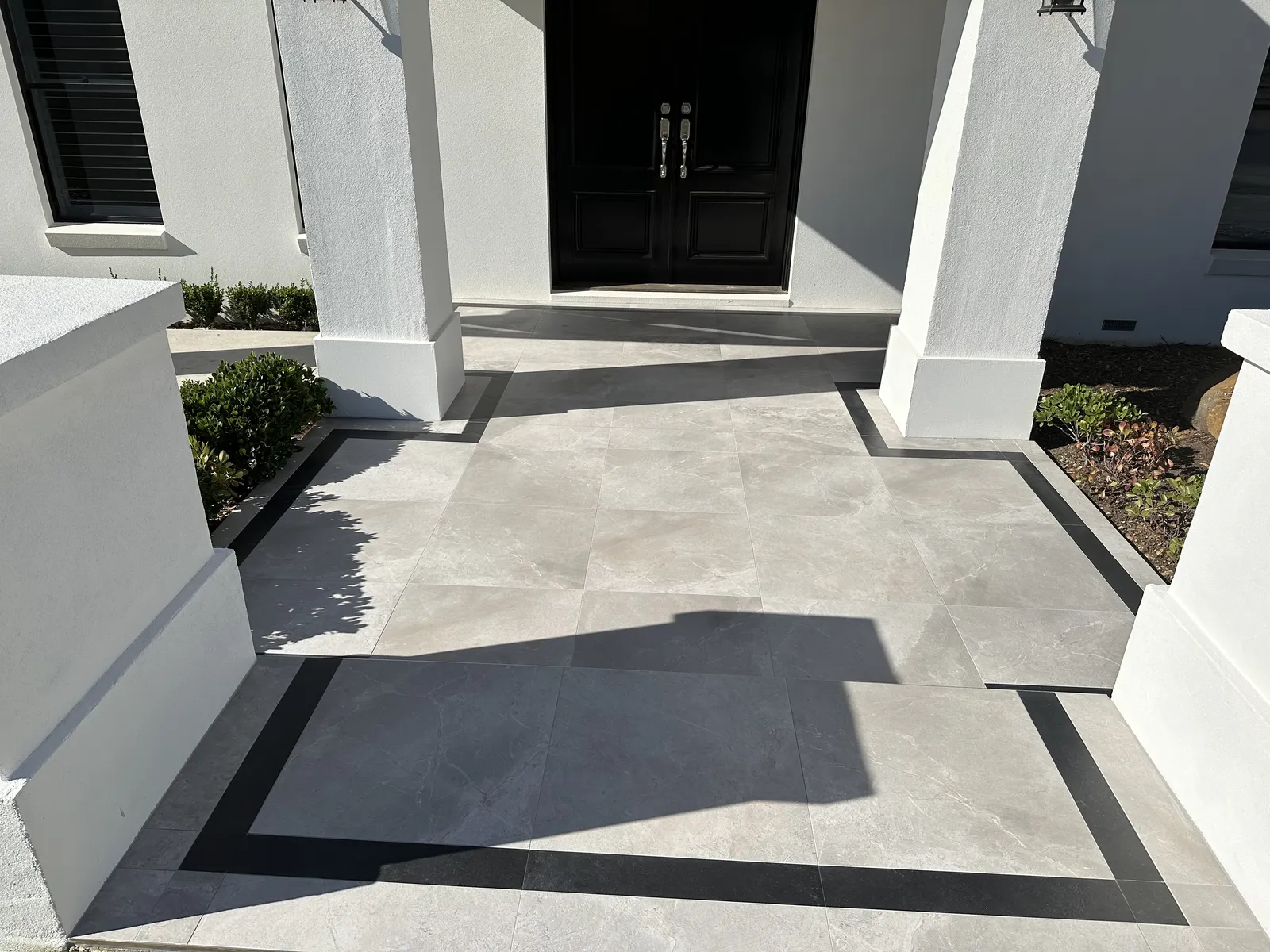 Front entrance porch paved with grey large-format porcelain tiles and dark border