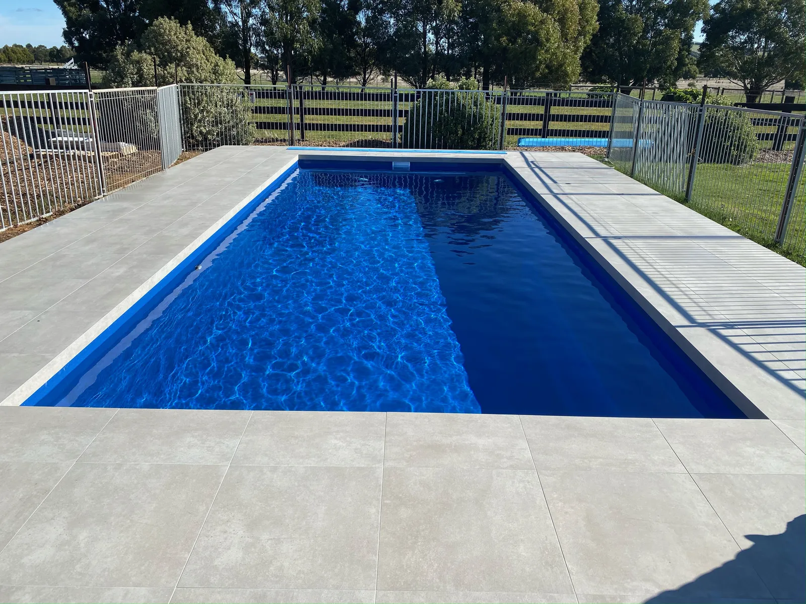 Inground pool with grey porcelain paver surround in a rural backyard