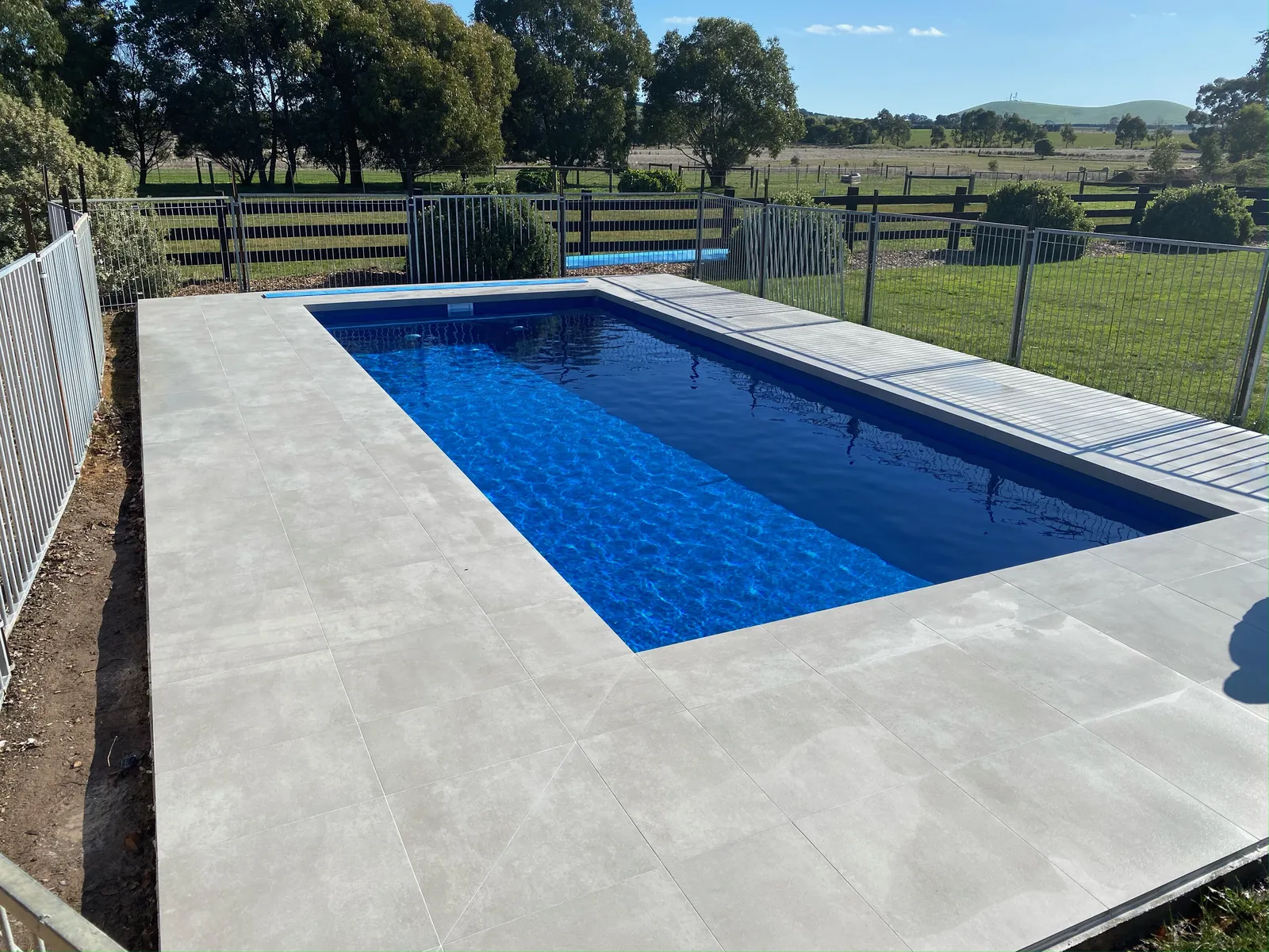 Inground pool with paved surround and post-and-rail fencing