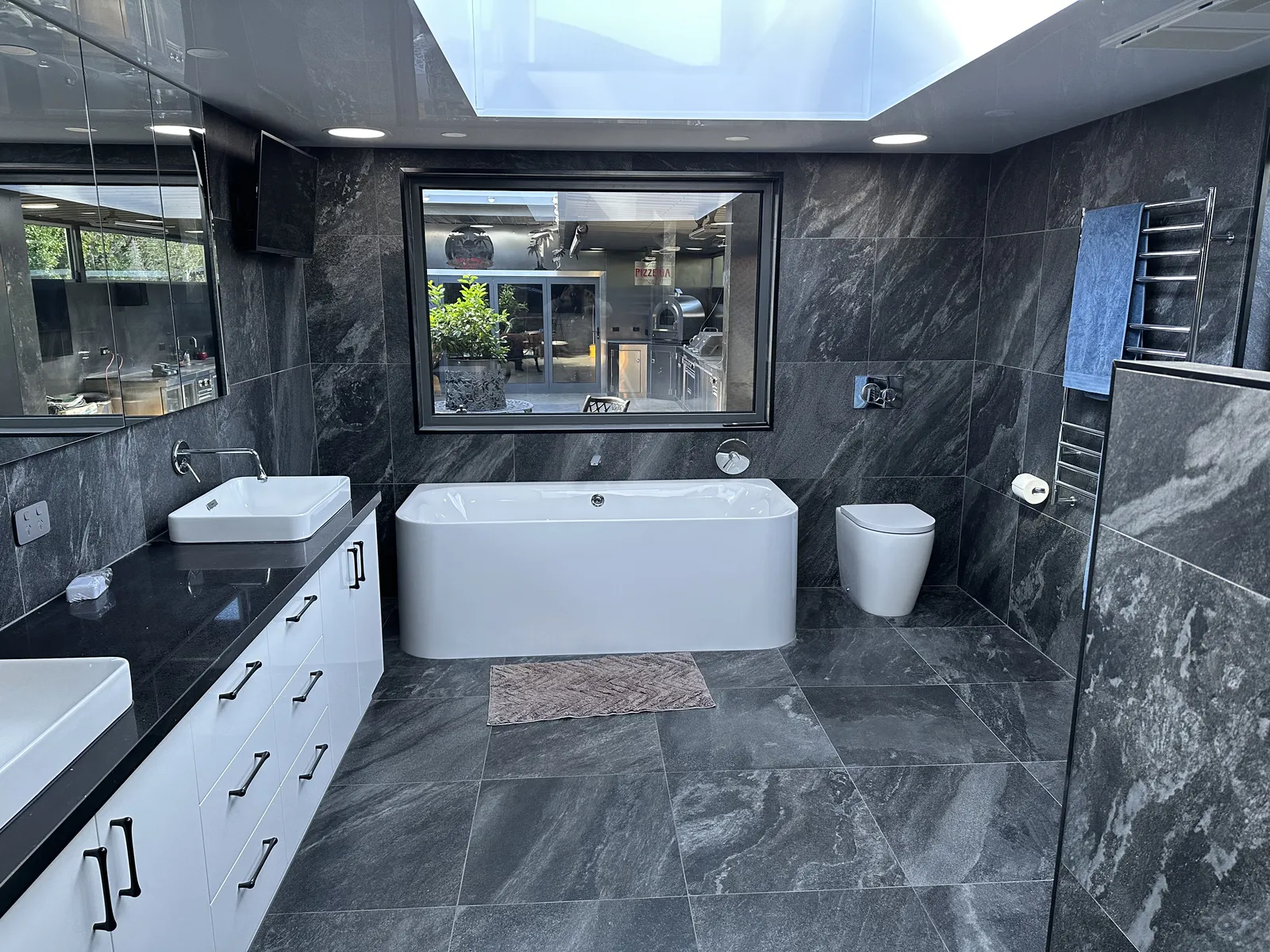 Bathroom with dark marble-look porcelain walls and floor, freestanding bath and twin vanity