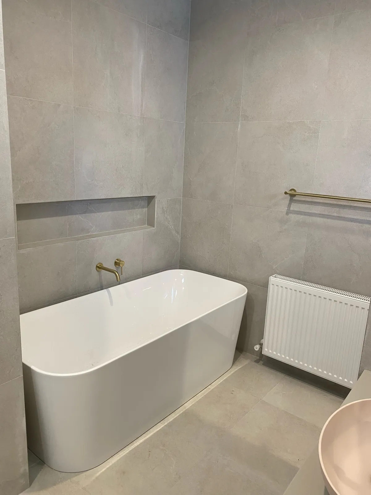 Bathroom with freestanding bath, grey large-format floor and wall tiles and brushed gold tapware