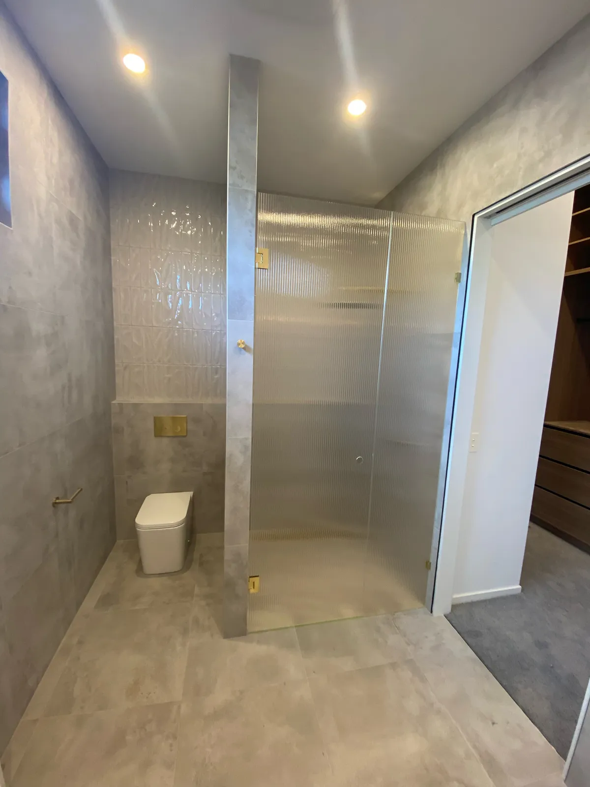 Walk-in shower with reeded glass screen, travertine-look tiles and gold accents