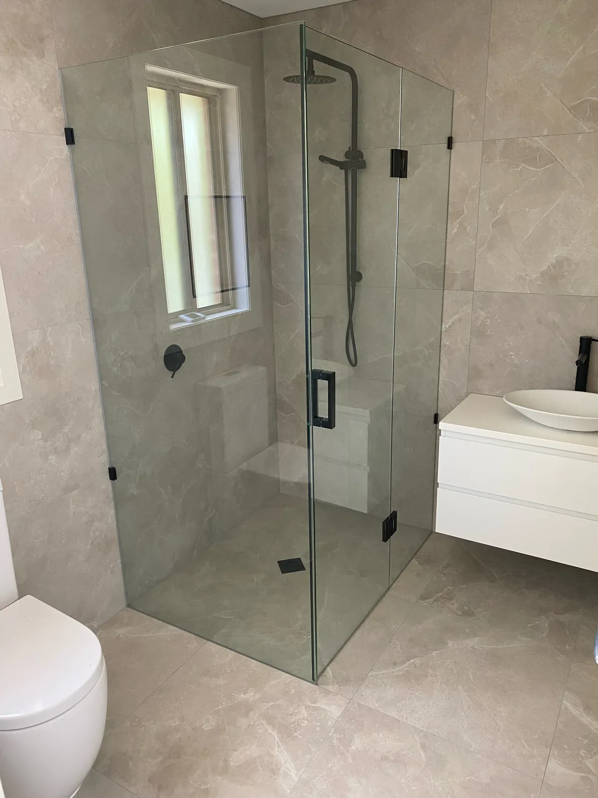 Frameless glass shower with marble-look large-format porcelain wall tiles and black tapware