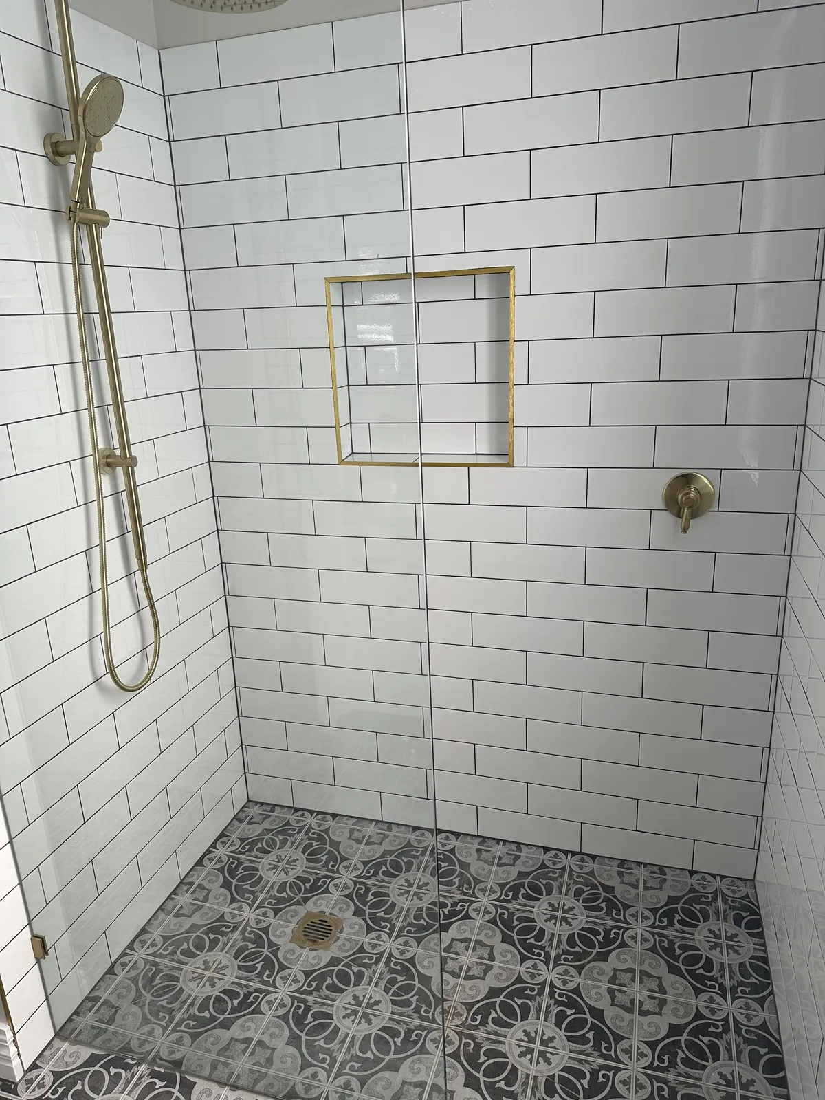 Walk-in shower with white subway wall tiles, patterned encaustic-look floor and gold tapware